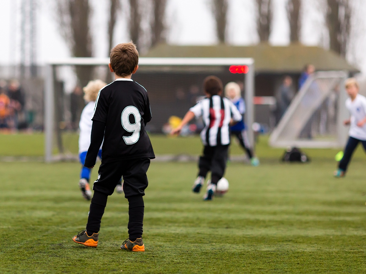 youth soccer player standing while other players run and play